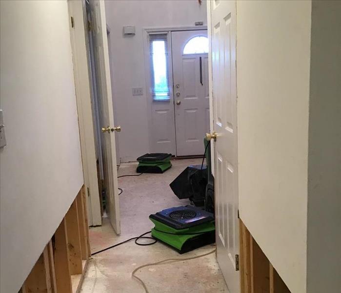 Two air movers near a dehumidifier in a hall with removed baseboards and lower drywall
