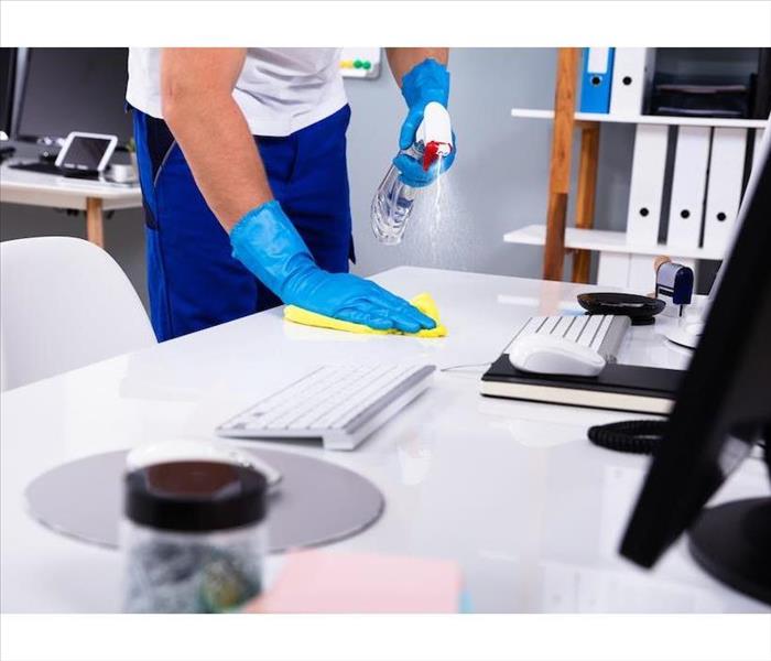 male wearing blue gloves, spraying a white desk with a liquid